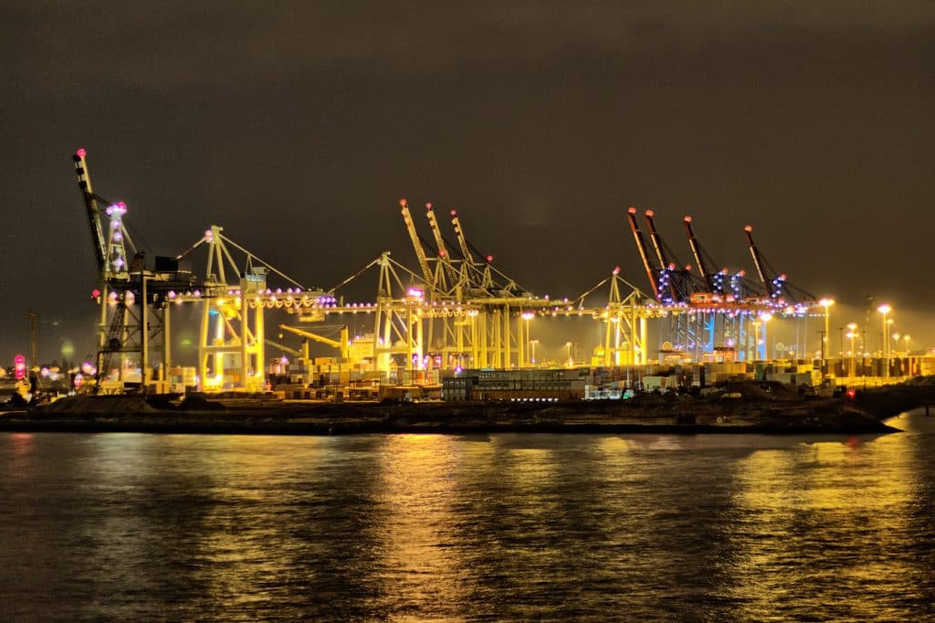 Container terminal with gantry cranes lit up at night, reflected in the water