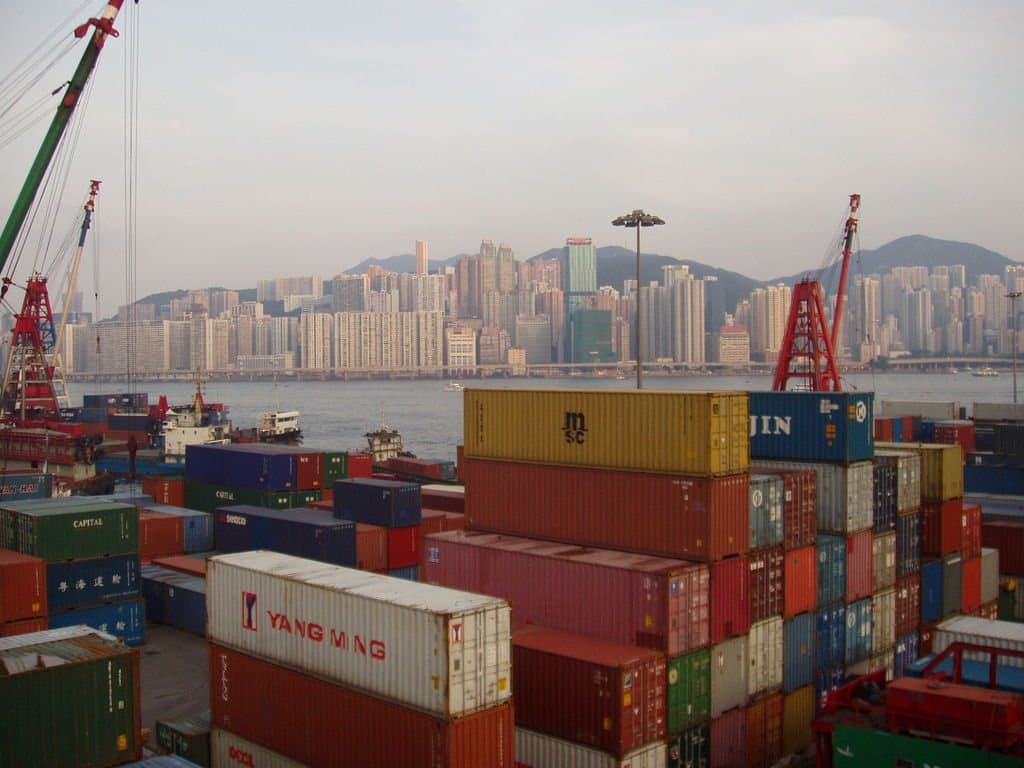 Stacked shipping containers at a terminal with the city skyline behind