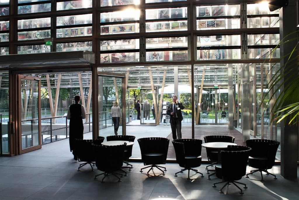 Glass atrium lobby of a conference venue with lounge chairs and delegates in business dress