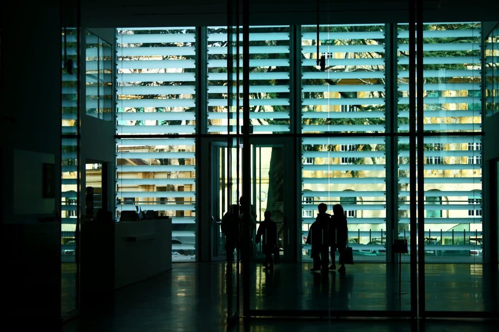 Illuminated glass facade of an office building at night with silhouettes in the lobby